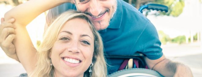 Partnersuche mit Handicap: Mann im Rollstuhl zusammen mit seiner Partnerin beim Selfie machen.