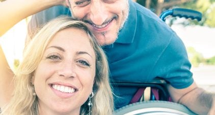 Partnersuche mit Handicap: Mann im Rollstuhl zusammen mit seiner Partnerin beim Selfie machen.