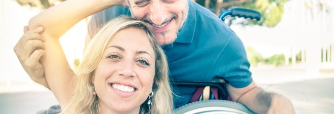 Partnersuche mit Handicap: Mann im Rollstuhl zusammen mit seiner Partnerin beim Selfie machen.