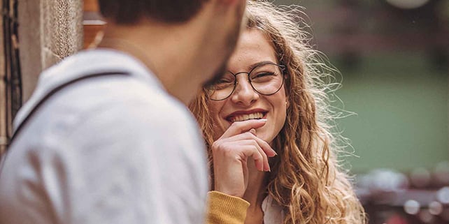 Frau mit Brille lacht in Richtung eines Mannes