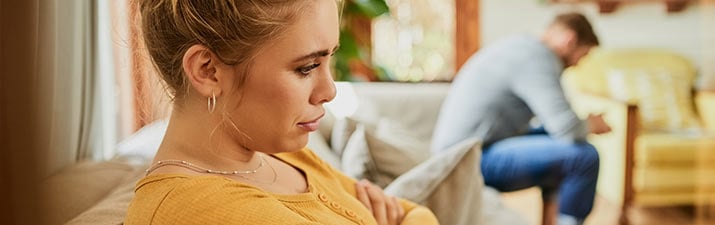 Frau und Mann erleben einen Beziehungskiller und sitzen frustriert voneinander entfernt im Wohnzimmer