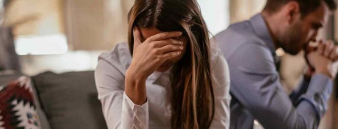 Frau stützt ihre Hand an die Stirn und hat Schuldgefühle nach der Trennung von ihrem Mann der verzweifelt hinter ihr sitzt