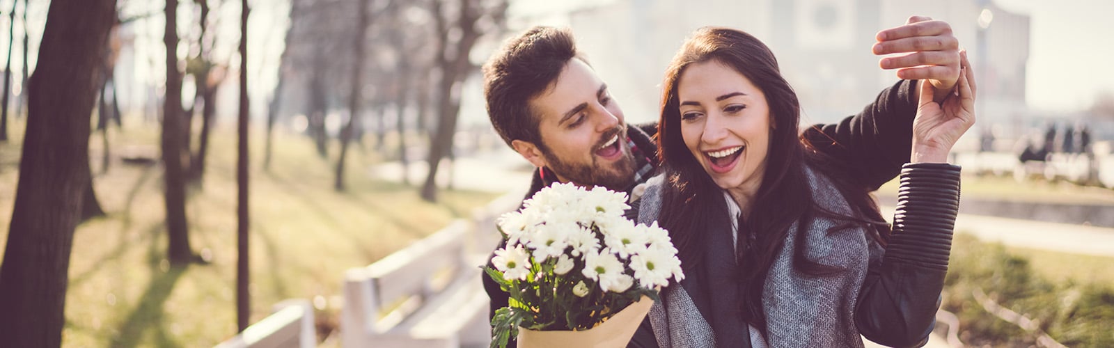 Mann mit Bart übergibt Frau weiße Blumen, beide lachen