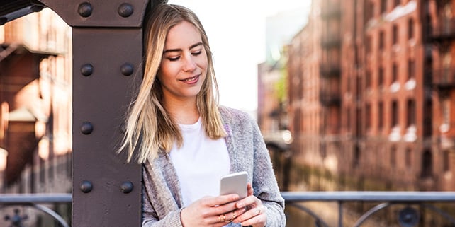 Blonde Frau schaut lächelnd auf Smartphone