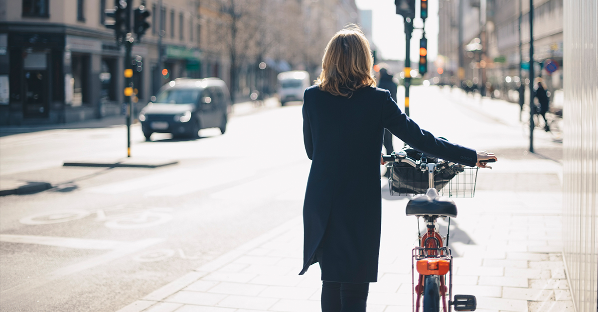 Frau läuft alleine durch Straße und schiebt dabei ein Fahrrad