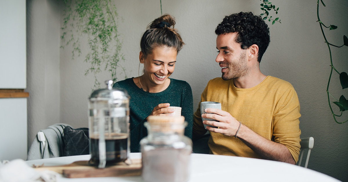 Mann und Frau sitzen gemeinsam im Café. Der Mann blickt die Frau an, sie schaut verunsichert nach unten