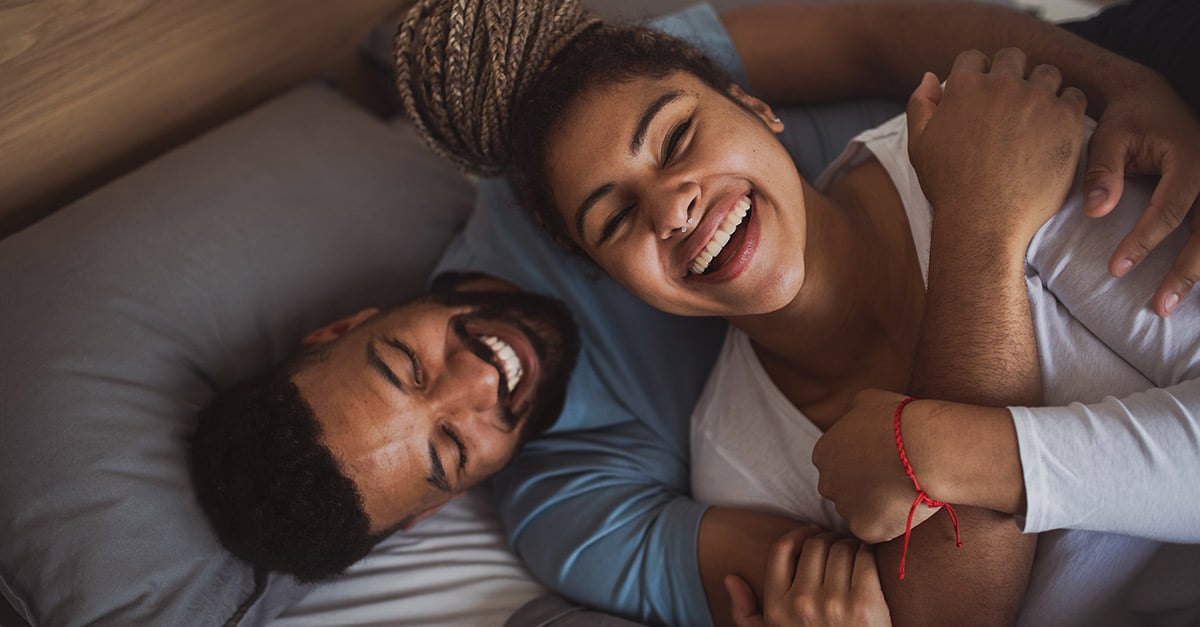 Frau und Mann liegen ich umarmend auf dem Bett, lachen und hören Musik.