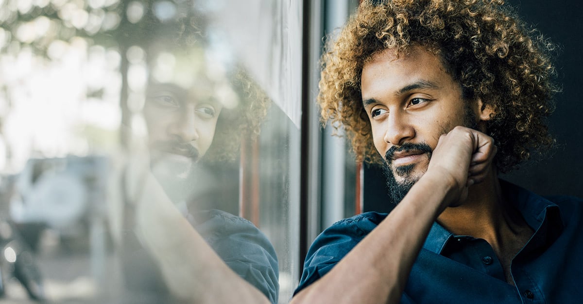 Mann mit braunen Locken blickt aus dem Fenster in die Ferne