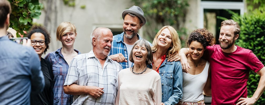 Eine Familie mit älteren und jüngeren Menschen steht gut gelaunt zusammen - von ihnen wird ein Foto gemacht.