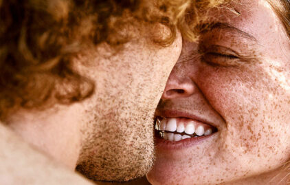 Rothaarige Frau mit Sommersprossen grins Mann mit Locken an