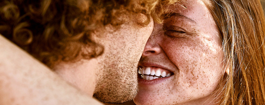 Rothaarige Frau mit Sommersprossen grins Mann mit Locken an