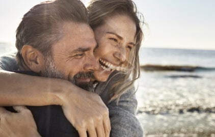 Ein Mann und eine Frau lachen gemeinsam, das Meer im Hintergrund.