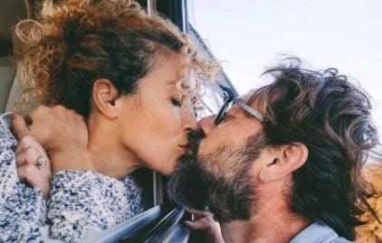 Frau und Mann küssen sich durch ein geöffnetes Autofenster.