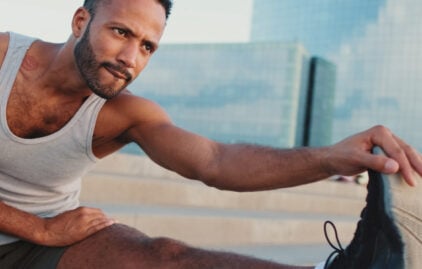 Ein POC-Mann in Sportkleidung macht eine Dehnübung und schaut dabei in die Ferne.