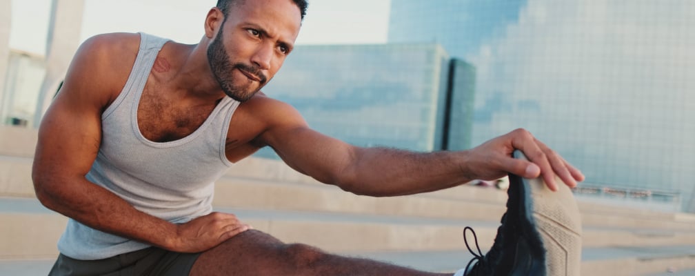 Ein POC-Mann in Sportkleidung macht eine Dehnübung und schaut dabei in die Ferne.