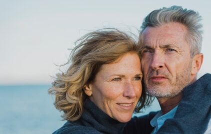 Ein Mann und eine Frau umarmen sich, im Hintergrund ist das Meer.