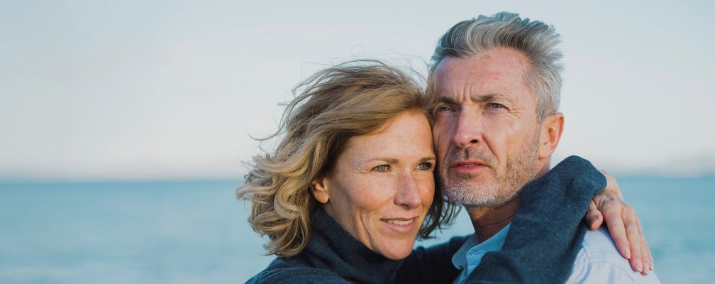 Ein Mann und eine Frau umarmen sich, im Hintergrund ist das Meer.