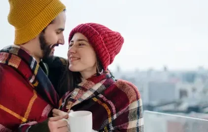 Paar kuschelt im Winter unter einer Decke und hält warme Teetassen in den Händen