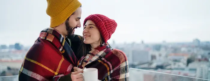 Paar kuschelt im Winter unter einer Decke und hält warme Teetassen in den Händen